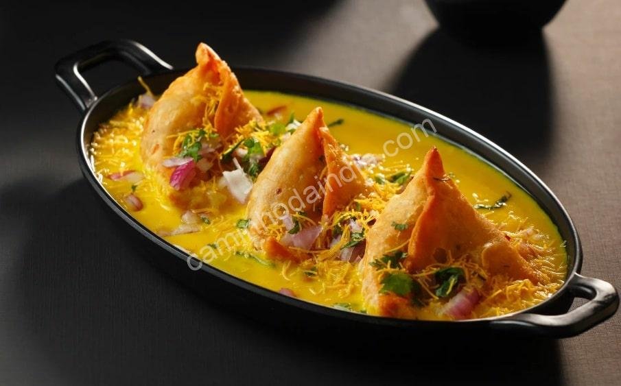 Samosa mergulhada em um molho de curry cremoso e cheio de sabor, uma variação deliciosa da receita tradicional