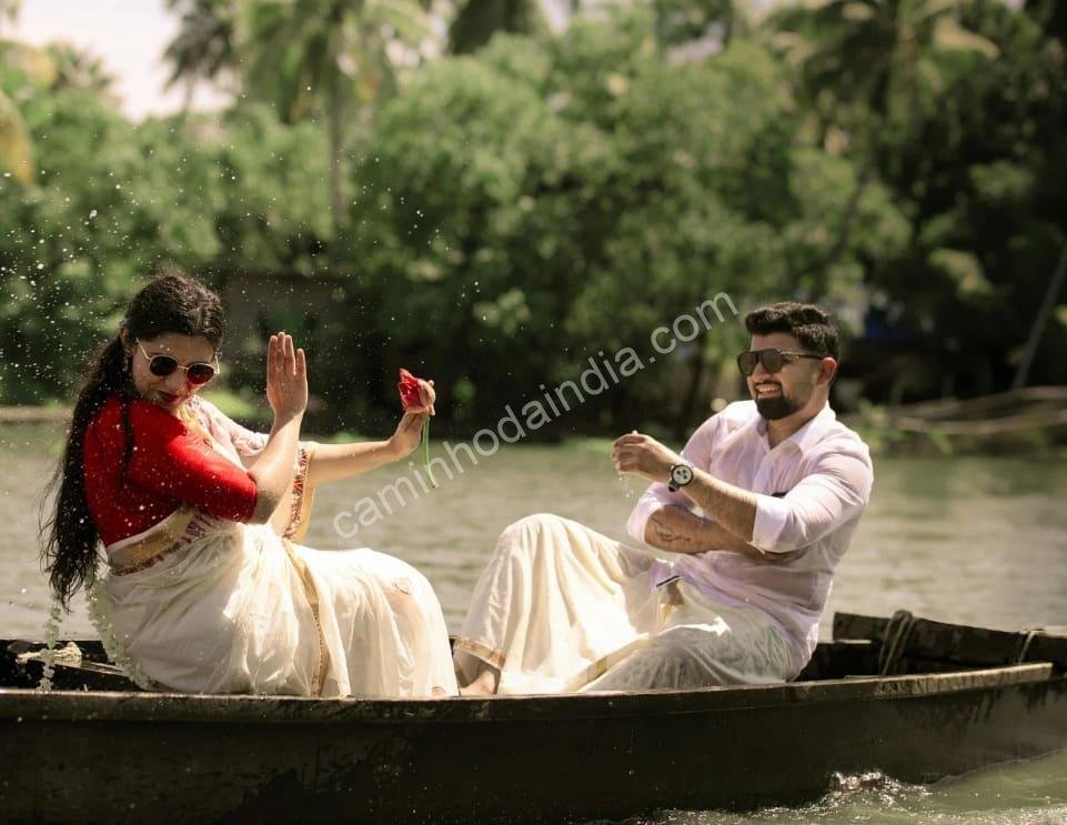casal-kerala-barco-rios-tradicional Um casal vestindo trajes tradicionais de Kerala — kasavu mundu e kasavu saree — navega serenamente pelos remansos, símbolo da beleza e cultura do estado