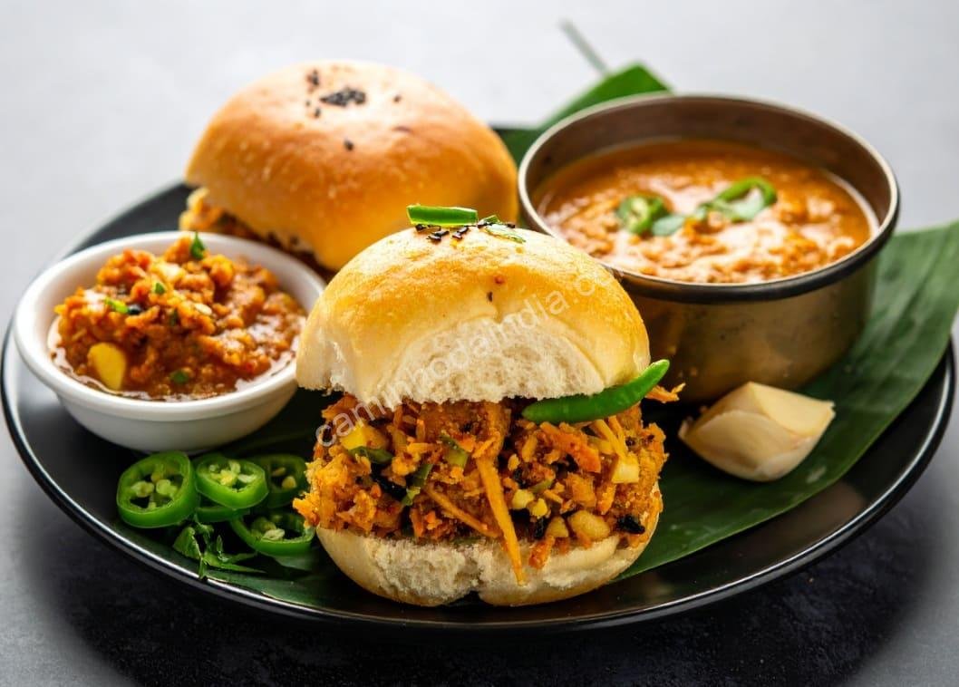 vada-pav-servido-em-restaurante-com-ingredientes-extras Vada pav gourmet servido em restaurante, acompanhado de chutneys, cebola e pimentas — uma versão moderna do lanche de rua mais amado de Mumbai